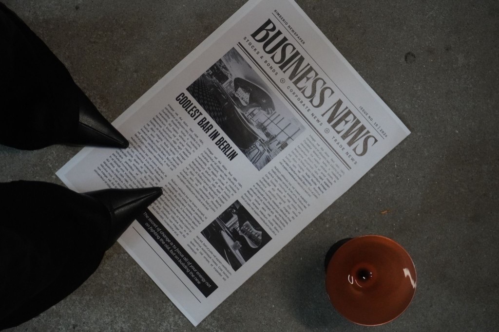 Editorial still: Business News newspaper, black heels and a glass on concrete