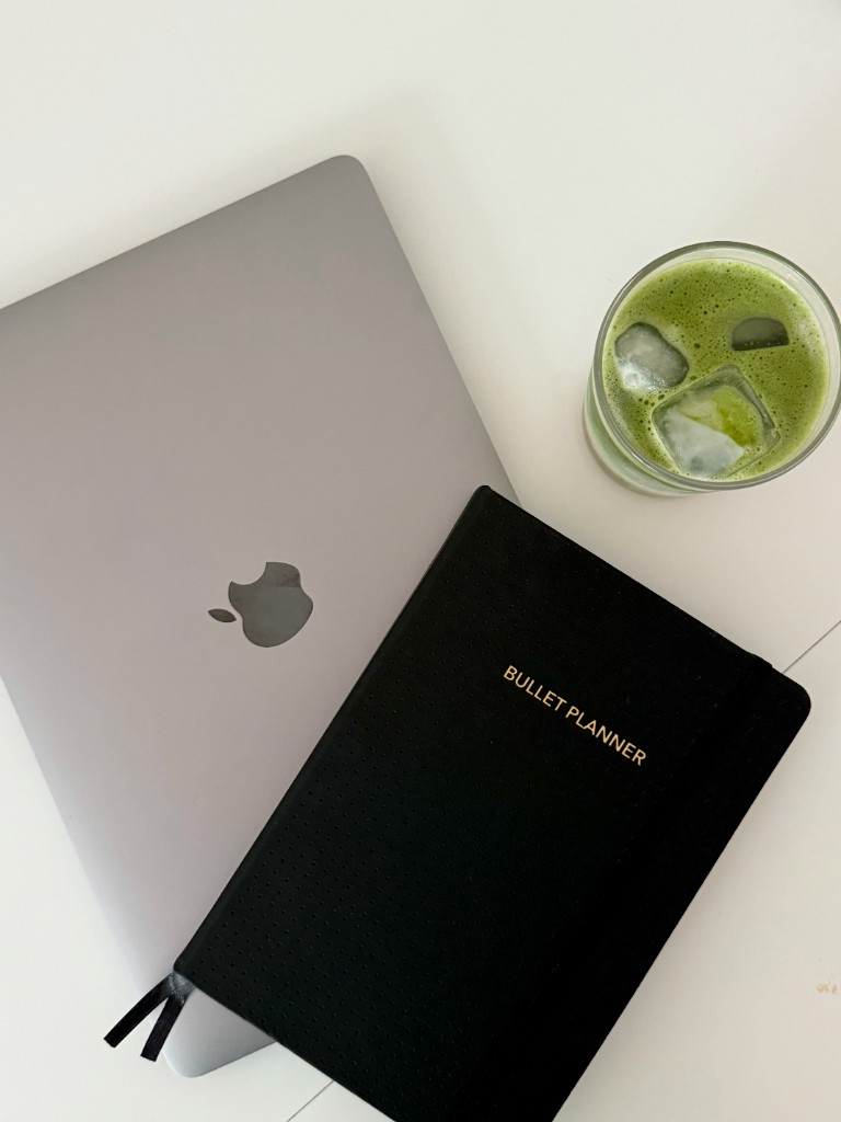 Laptop, bullet planner and iced matcha on a white studio desk